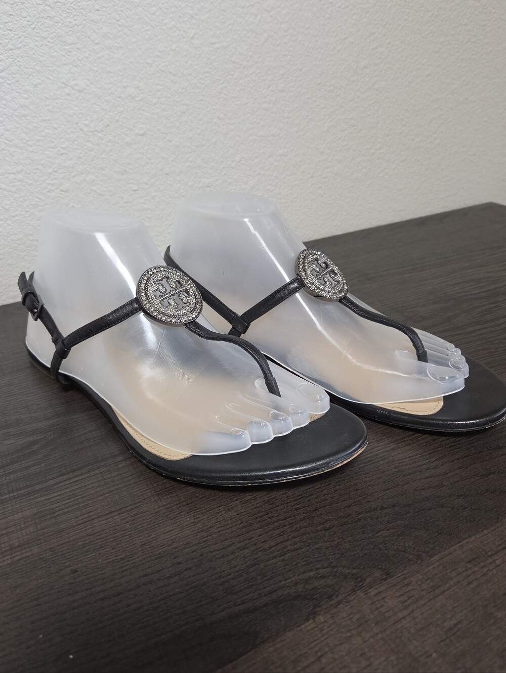 Tory Burch Black T-Strap Sandals with Silver Rhinestone Emblem Accents.